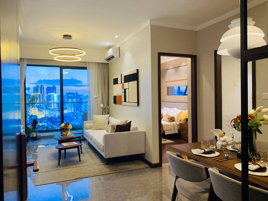 Modern apartment interior at Agile Sky Residence with a living room, dining area, and bedroom. A large window frames a sunset cityscape. Neutral tones, contemporary furniture, and decorative lighting create a cozy, stylish atmosphere.