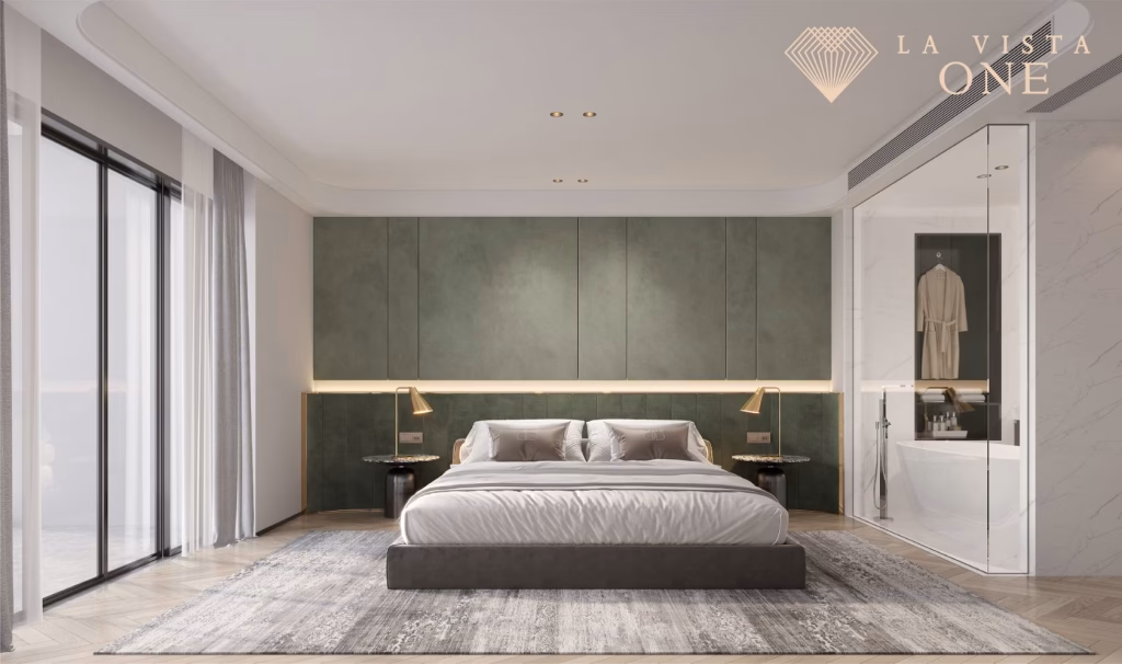 Modern bedroom in a luxury penthouse featuring a large bed, green accent wall, bedside tables and lamps, floor-to-ceiling windows with sheer curtains, glass-walled bathroom, and the La Vista One logo in the upper right corner.