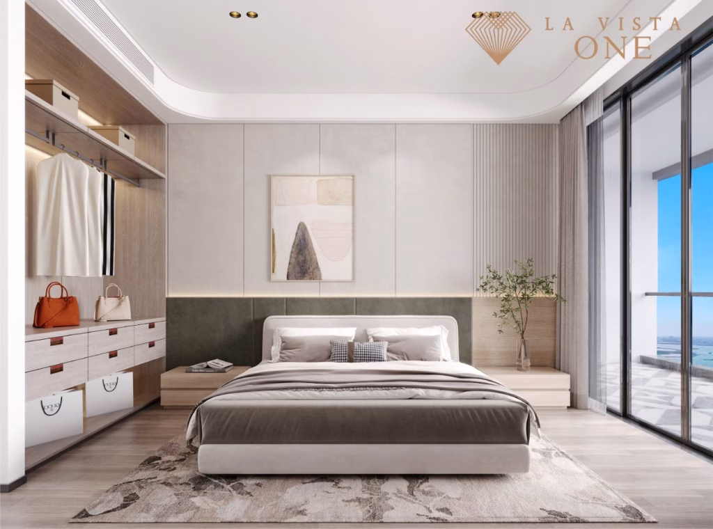 Modern, minimalist bedroom in a luxury penthouse with a large bed, soft neutral colors, open closet with shelves and handbags, wall art above the bed, floor-to-ceiling windows, and a scenic outdoor view. La Vista One logo in the corner.