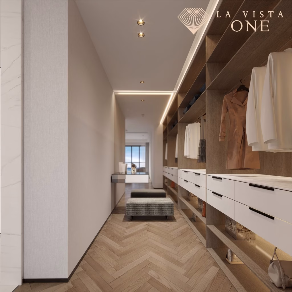 A modern walk-in closet with wooden shelves, white drawers, and hanging clothes evokes the feel of a luxury penthouse. A bench sits in the center, and a window at the end lets in natural light. LA VISTA ONE is written in the top right corner.