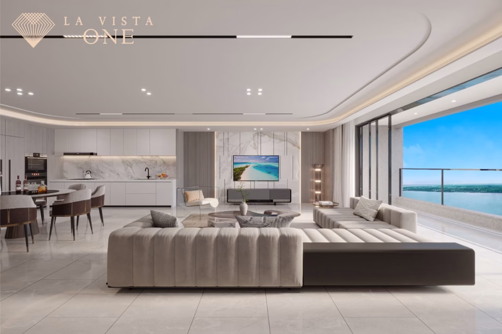 Luxurious modern living room at La Vista One featuring a large gray sectional sofa, dining area, open kitchen, and floor-to-ceiling windows with ocean views. The La Vista One logo is in the top left corner.
