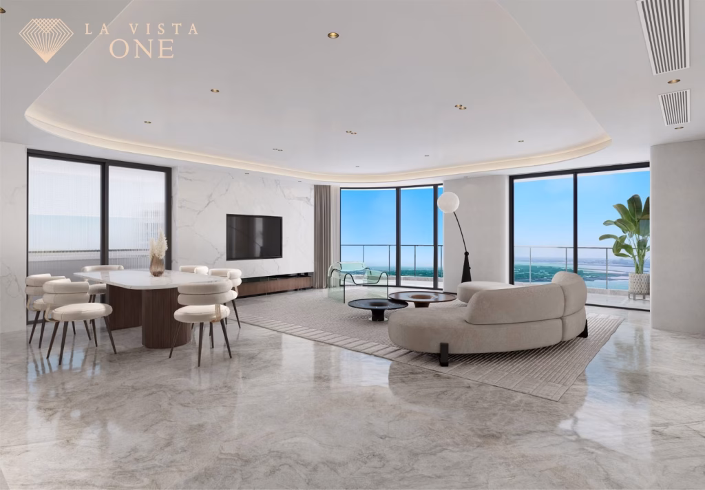 Modern, spacious Riverside Penthouse living and dining area with marble floors, large windows showing ocean views, a curved sofa, round dining table with chairs, and minimalist decor; La Vista One logo in the top left corner.