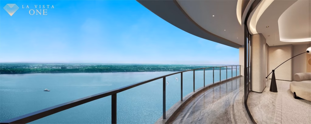 Spacious modern balcony of this Riverside Penthouse features a glass railing overlooking a wide, calm river and distant green shoreline under a clear blue sky. Interior includes elegant curved walls and a cozy seating area.