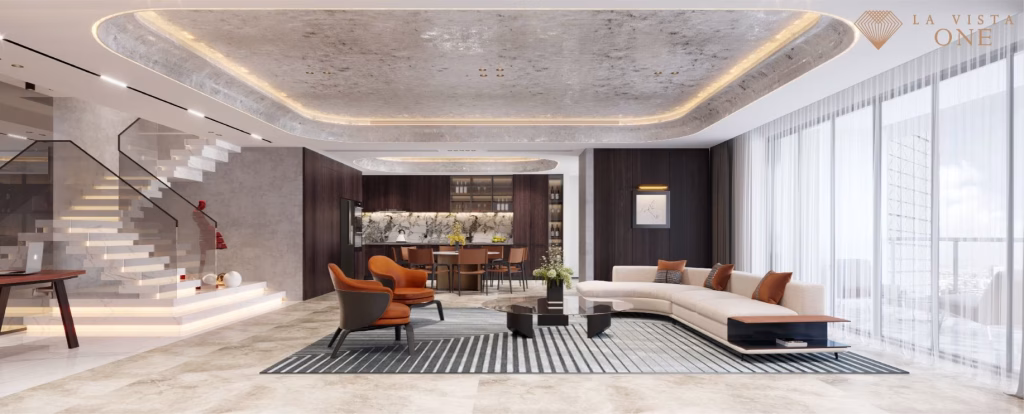 Modern, spacious living room at La Vista One with large windows, a curved beige sofa, orange chairs, a striped rug, and a stylish marble staircase. The room features luxurious finishes and an open kitchen in the background.