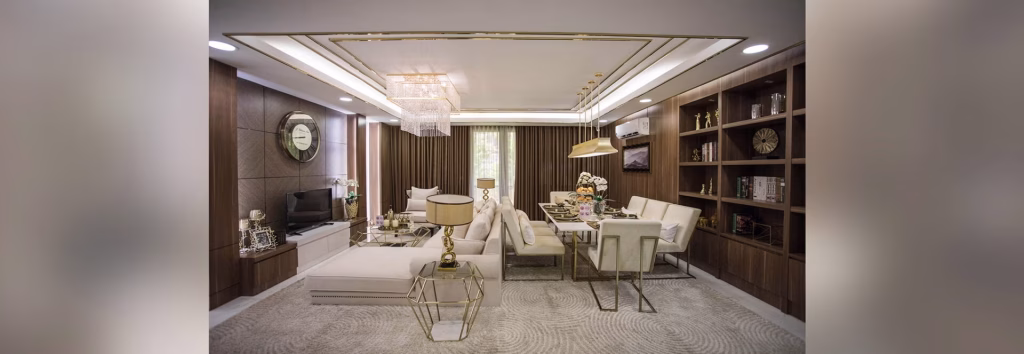Modern living and dining area at Orkide The Royal with white and beige furniture, a glass dining table, built-in wooden shelves, a chandelier, and large windows with brown curtains, creating a stylish and cozy ambiance.