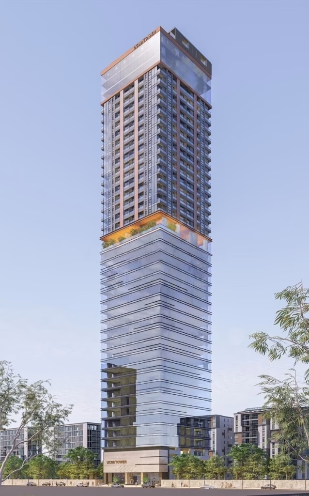 A modern high-rise building, the UC88 Tower studio features reflective glass windows, a wide lower section, and a slender upper tower with copper-colored details, surrounded by smaller buildings and trees under a clear sky.