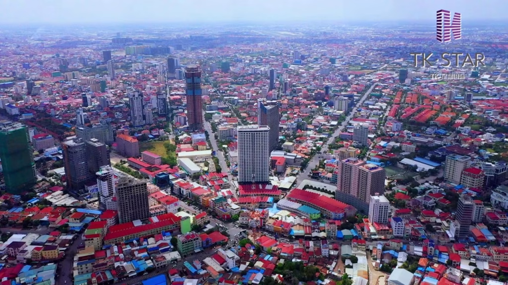 Aerial view of Star City’s dense cityscape with tall buildings, colorful rooftops, and grid-like streets under a clear sky. The TK Star logo appears in the top right corner.