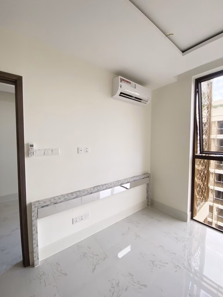 A bright, empty 1 bedroom condo featuring white marble floors, cream-colored walls, a split air conditioner above a marble-trimmed niche, and a large window that fills the space with natural light.