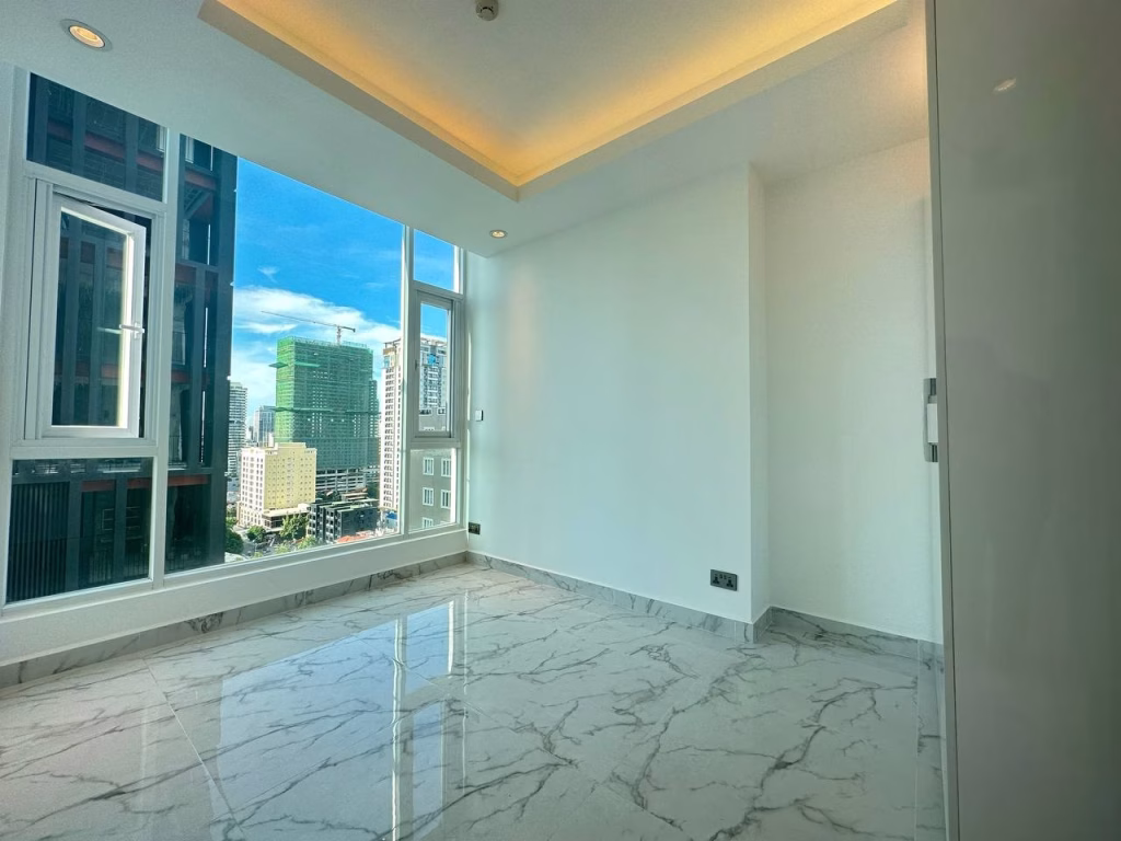 A bright, empty 2 bedroom apartment with marble flooring, white walls, and a large window offering a cityscape view under a blue sky. Recessed ceiling lighting adds a modern touch.