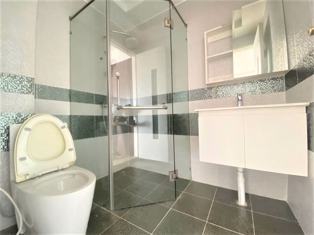Modern bathroom in a 2 bedroom condo featuring a glass shower enclosure, toilet with the lid up, white vanity with sink, wall-mounted mirror, and gray tile flooring and walls with horizontal decorative stripes.