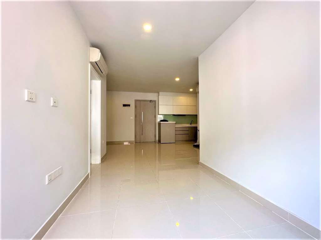 A bright, empty 2 bedroom condo with glossy tiled floors, white walls, ceiling lights, air conditioner, and a small modern kitchen area at the far end near a wooden door.