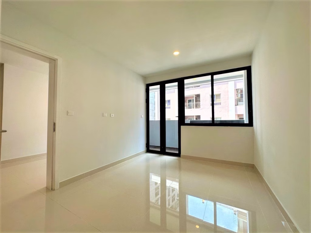 A bright, empty 2 bedroom condo with white walls, glossy tiled floors, and a large window and glass door leading to a balcony, flooding the space with natural light. An open doorway leads to another room.