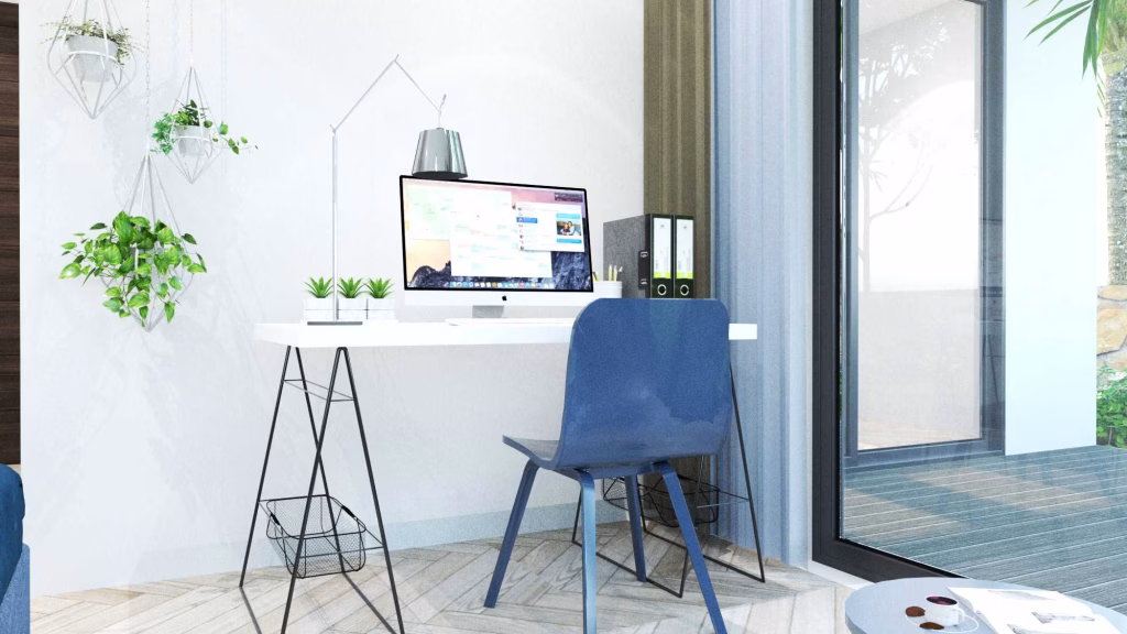 A modern, bright home office in Oasis Harmony villas features a white desk, blue chair, computer monitor, potted plants, hanging planters, file folders, and a large glass door letting in natural light with views of a tree.