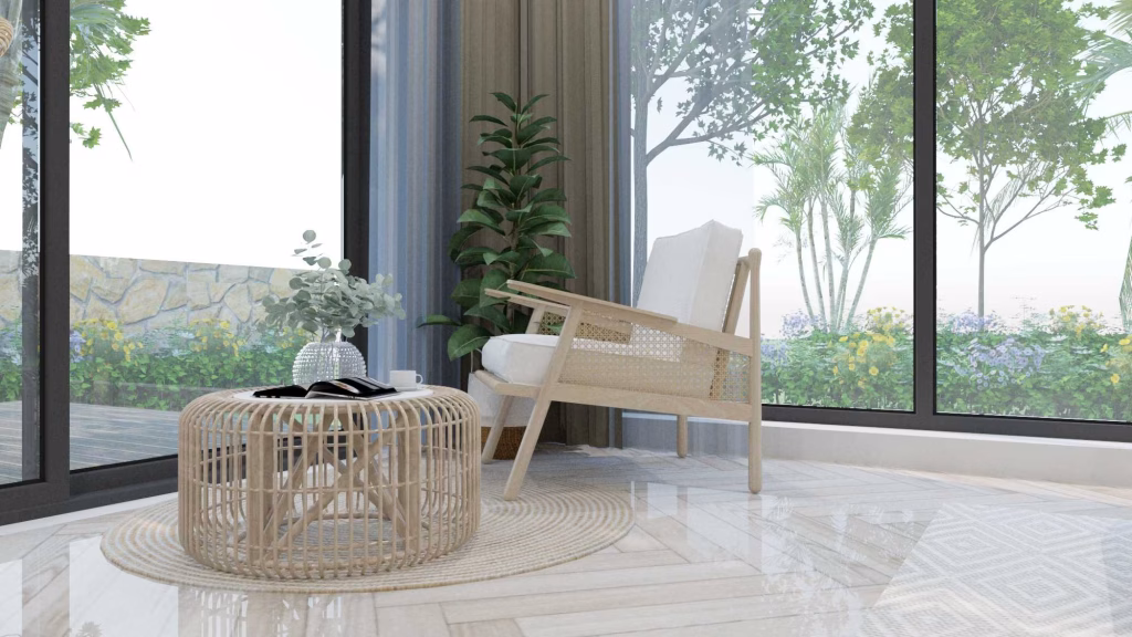 A cozy corner with a modern armchair and round wicker table topped with a vase and book, set on a light rug by large windows overlooking a green, sunlit garden—a perfect spot found in kampot homes for sale.