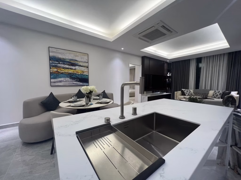 Modern open-concept living space in J Tower3 featuring a marble kitchen island and sink, a dining table with place settings, and a cozy living area with a sofa, TV, and stylish decorative artwork on the wall.
