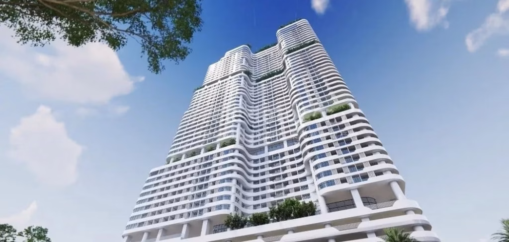 A modern high-rise building with curved white balconies and glass windows, viewed from below against a blue sky with scattered clouds and tree branches in the corners.