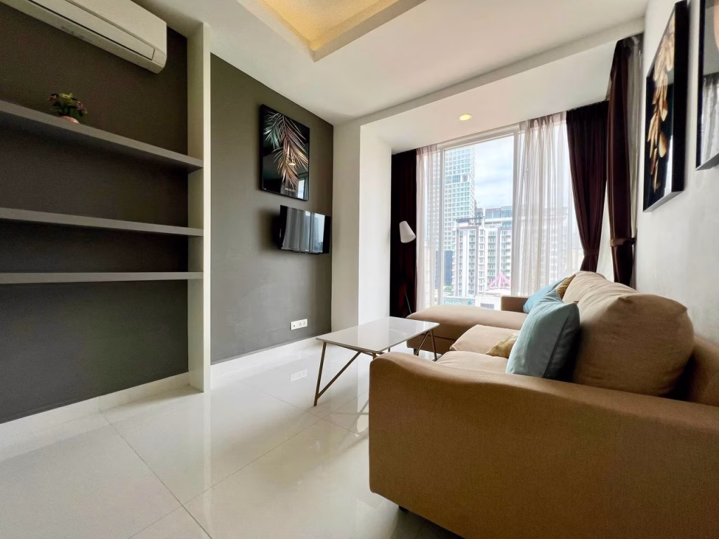 A modern studio apartment for rent featuring a beige sofa, glass coffee table, wall-mounted TV, empty shelves, large window with city view, and framed artwork on dark and white walls.