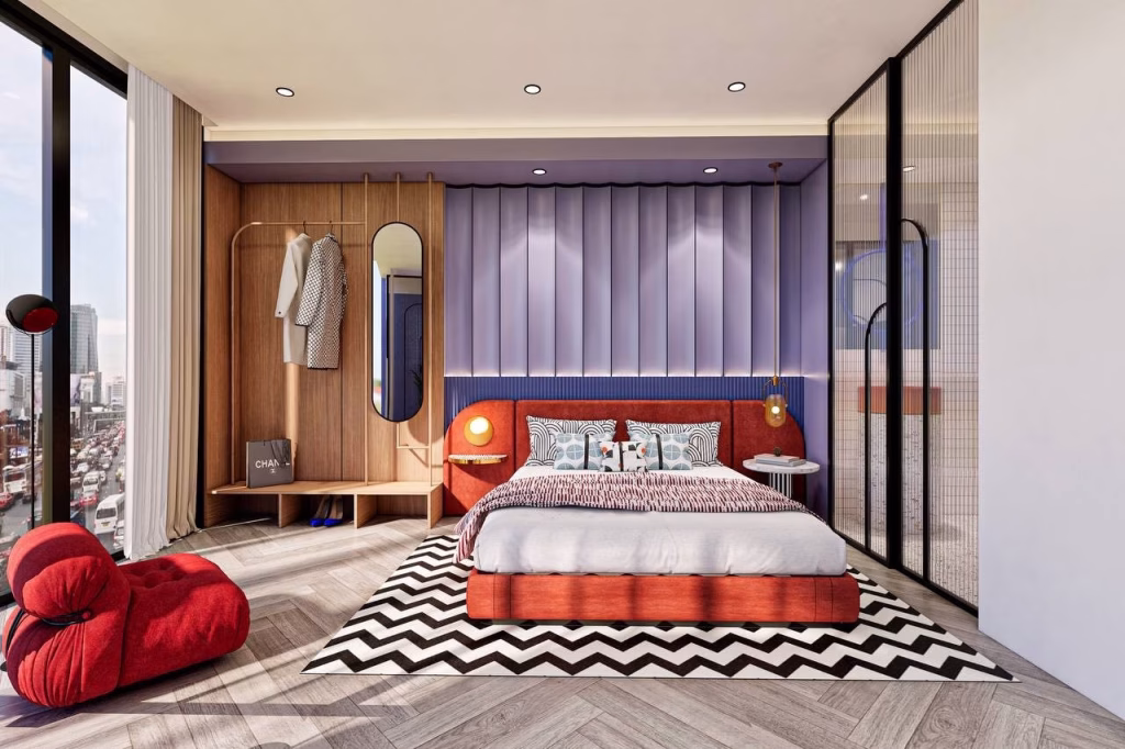 Modern bedroom with floor-to-ceiling windows overlooking the cityscape, a red lounge chair, chevron-patterned rug, platform bed with patterned pillows, and a wooden wall panel with mirror—just minutes from Time Square 6.