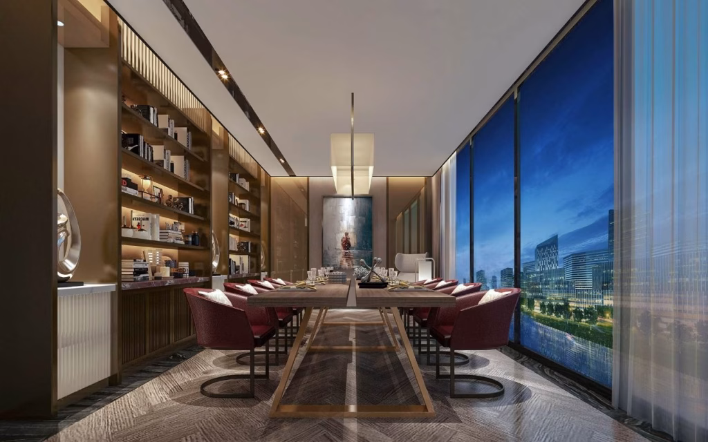 A modern, elegant dining room with a long table, red chairs, built-in bookshelf, and large floor-to-ceiling windows showcasing a riverfront luxury cityscape with illuminated buildings at night.