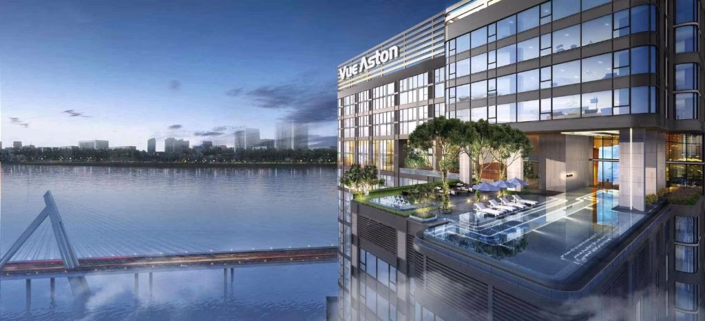 Modern riverfront luxury Westin high-rise with an outdoor infinity pool and lounge area on an upper floor overlooking the river, city skyline, and a cable-stayed bridge at dusk.