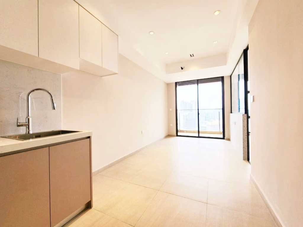 A modern, minimalistic 1 bedroom condo kitchen with light-colored cabinets, a stainless steel sink, and a spacious, bright living area featuring large windows and a glass door opening to a balcony with a stunning city view.