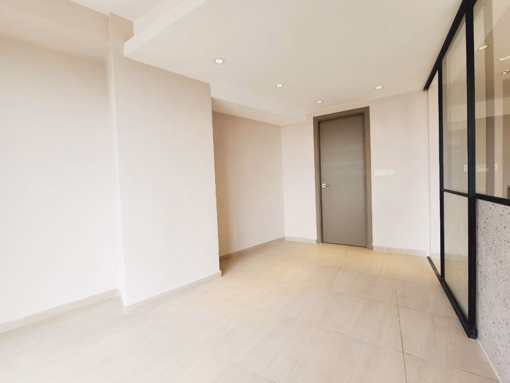 A bright, empty 1 bedroom condo featuring beige tiled floors, cream-colored walls, a closed gray door, recessed ceiling lights, and a glass wall with black frames on the right side.