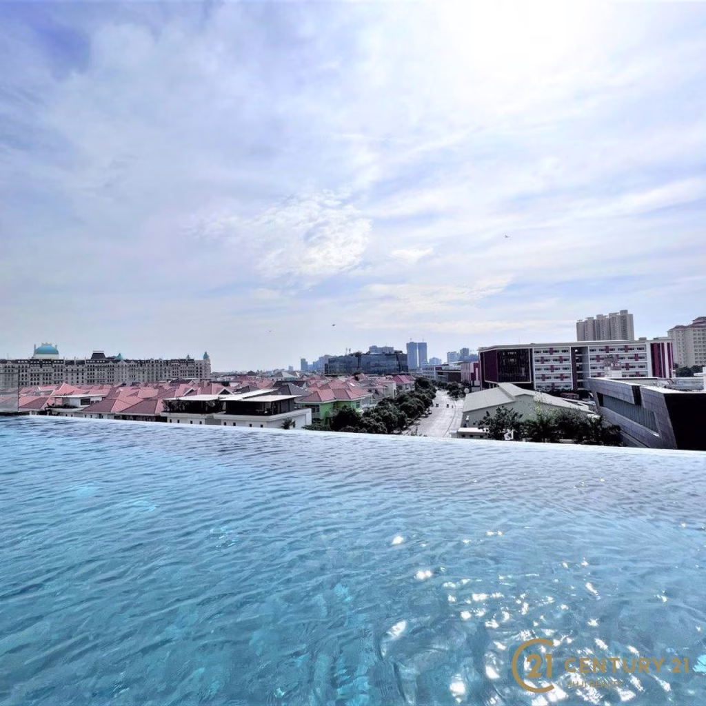 Infinity pool with clear blue water at Meridian Koh Pich, overlooking a cityscape of mid-rise and high-rise buildings under a bright, partly cloudy sky.