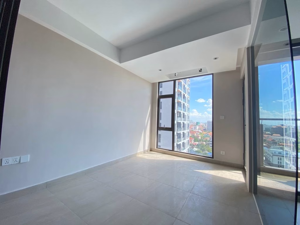 Bright, empty room at Time Square 3 Condo with large floor-to-ceiling windows, beige tiled floor, light walls, and a cityscape view beneath a blue sky with clouds; modern, minimalistic design.