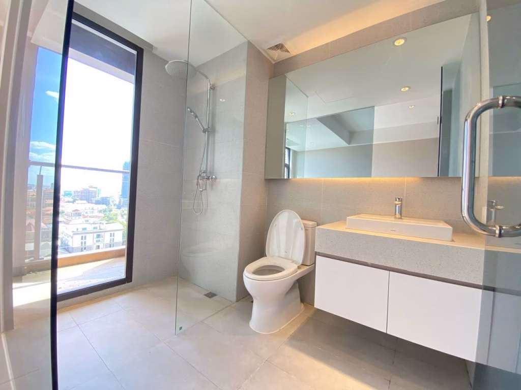 Modern bathroom at Time Square 3 Condo with large mirror, glass shower enclosure, white toilet, and floating vanity. Sunlight streams through a floor-to-ceiling window, creating a bright and spacious atmosphere.