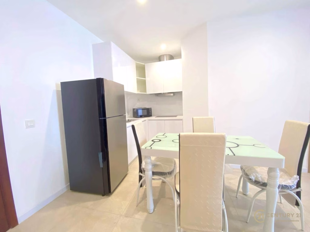 A modern kitchen in The Penthouse Residence features a black refrigerator, white cabinets, microwave, and a glass dining table with four cream-colored padded chairs on a light tile floor.