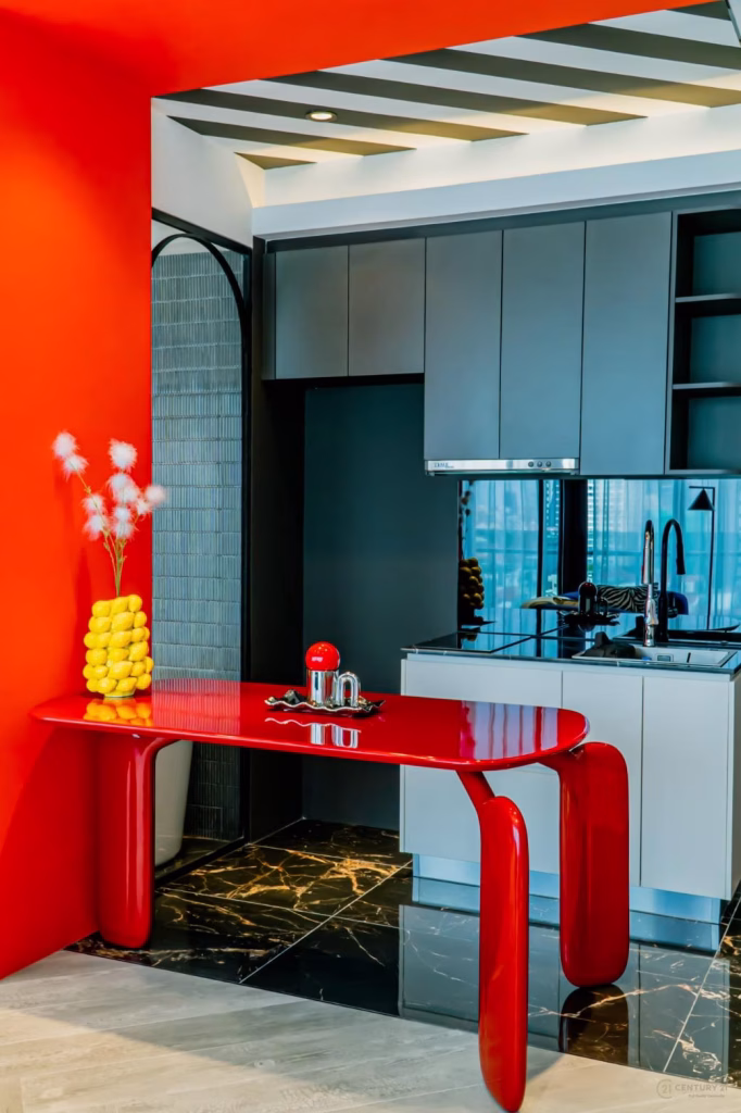 A modern kitchen in the Time Square 6 Project features sleek gray cabinets, a glossy red table, a vase with yellow spheres and white feathery stems, shiny black marble flooring, and bold red and white walls for a vibrant, contemporary look.