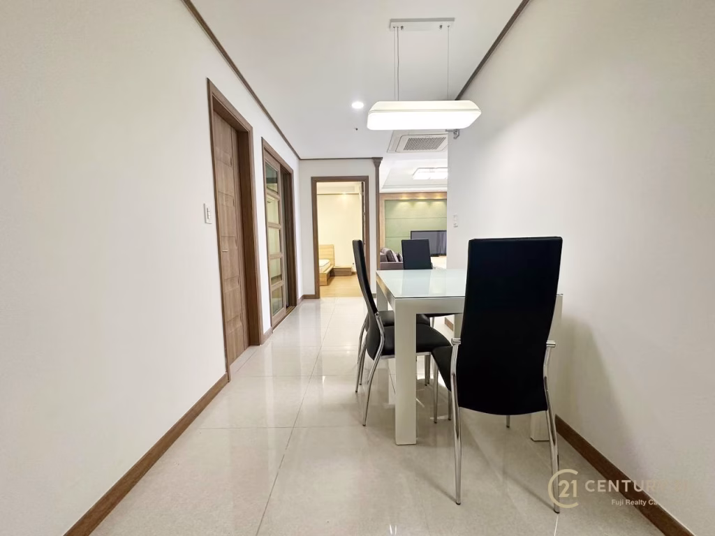 Modern dining area with a white table and four black chairs at De Castle Royal BKK1, positioned along a hallway with white walls and tiled floors; adjacent rooms visible in the background.