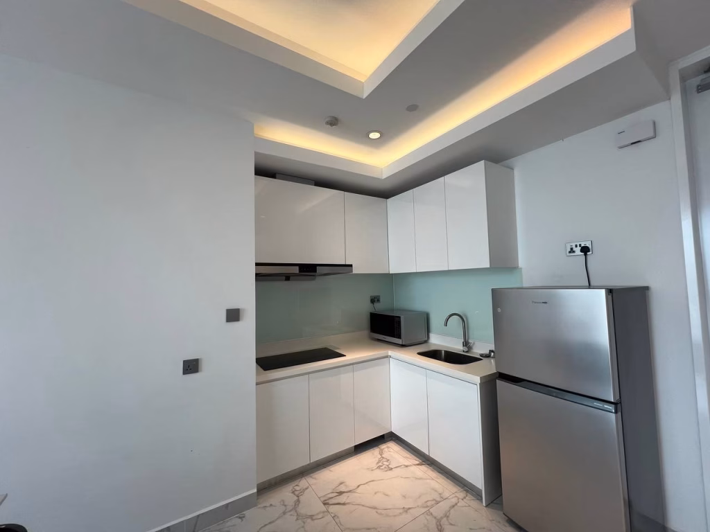 A modern kitchen in this 2 Bedroom Condo features white cabinets, a glass backsplash, under-cabinet lighting, an electric stove, microwave, stainless steel fridge, and marble-patterned floor tiles.